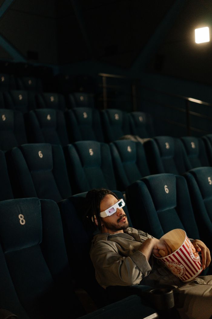 A man enjoys a movie alone in an empty theater, wearing 3D glasses and holding popcorn.